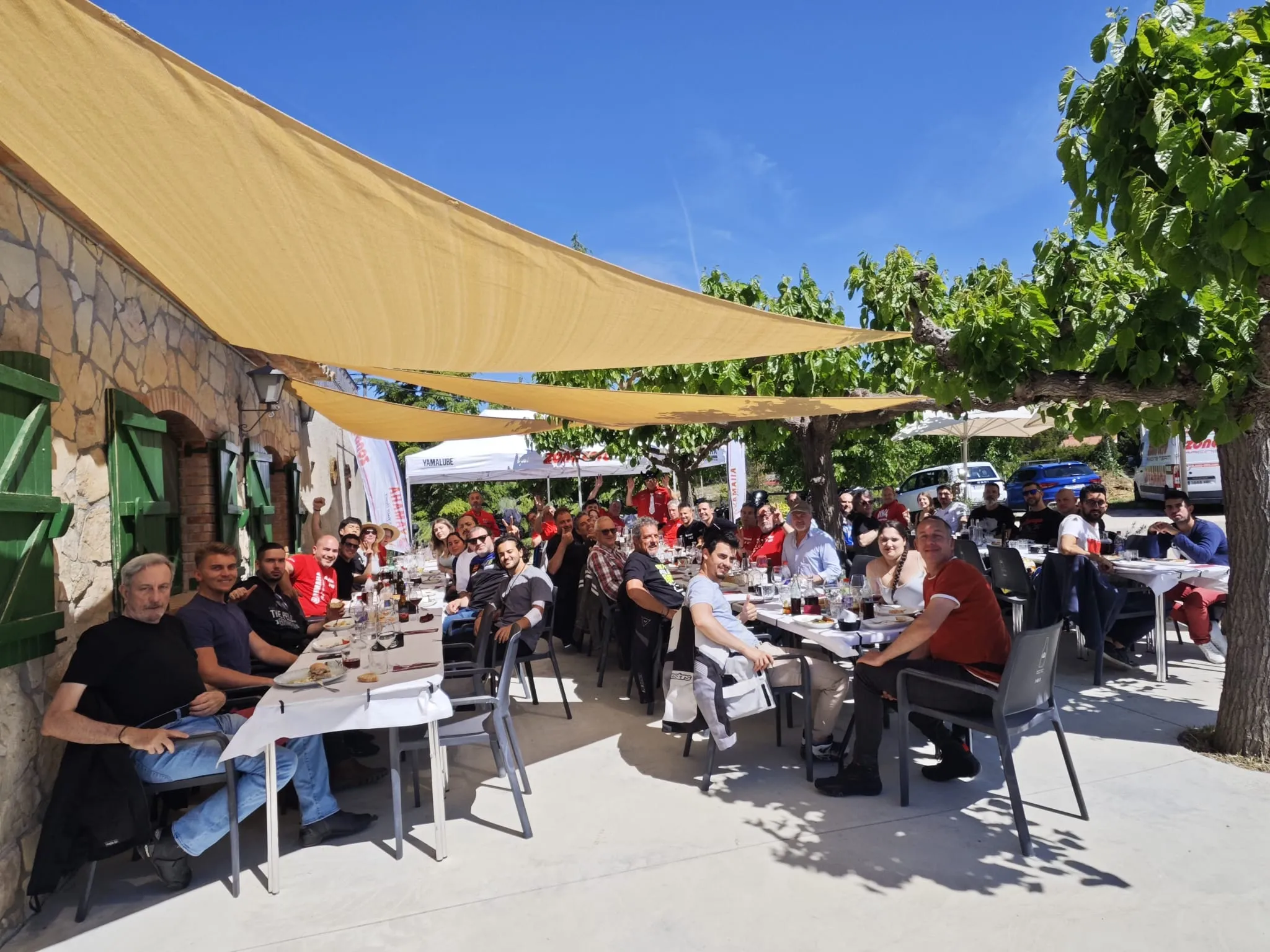 El grup dinant a taules llargues sota veles d’ombra, a la terrassa