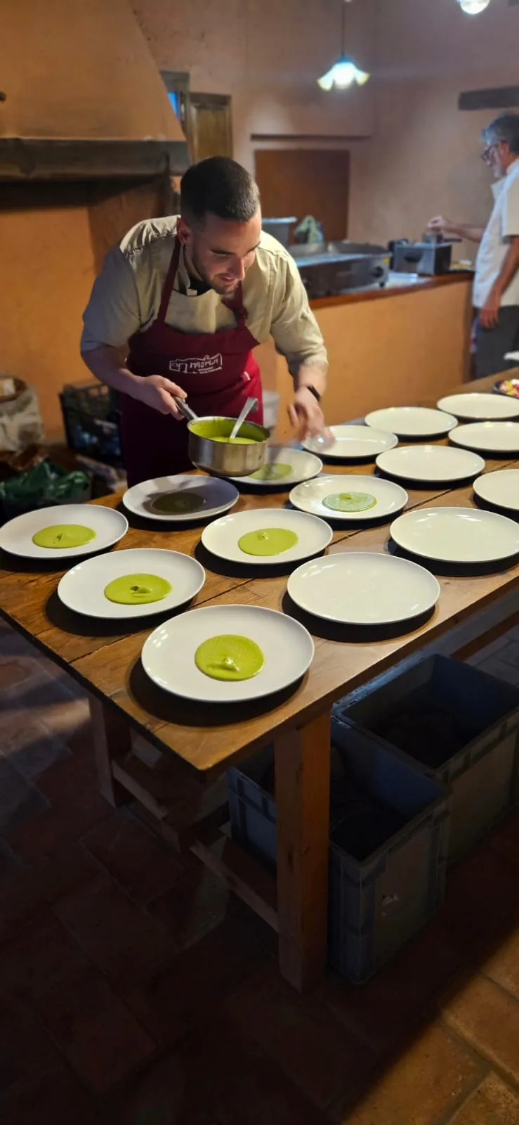 L’Adrián abocant una crema verda amb un cassó en una filera de plats