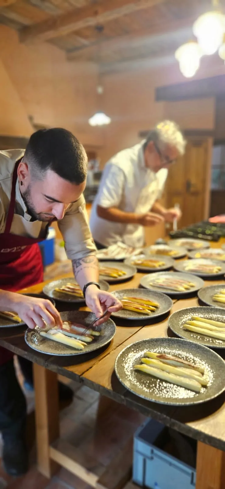 L’Adrián emplatant espàrrecs blancs en una filera de plats, a la cuina