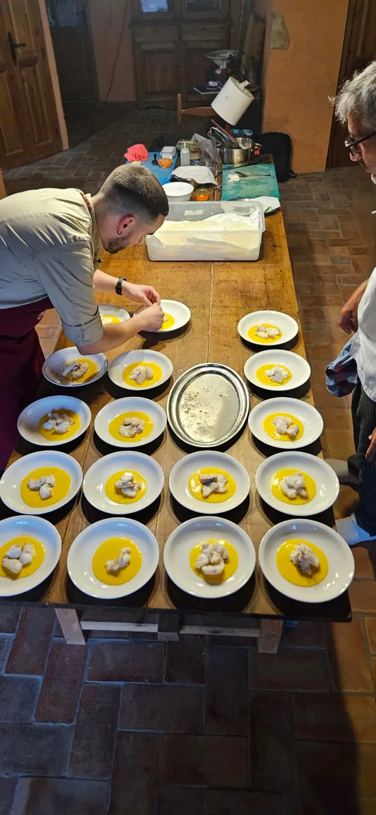 Una vintena de plats de peix sobre una crema groga, acabats d’emplatar en una taula de fusta