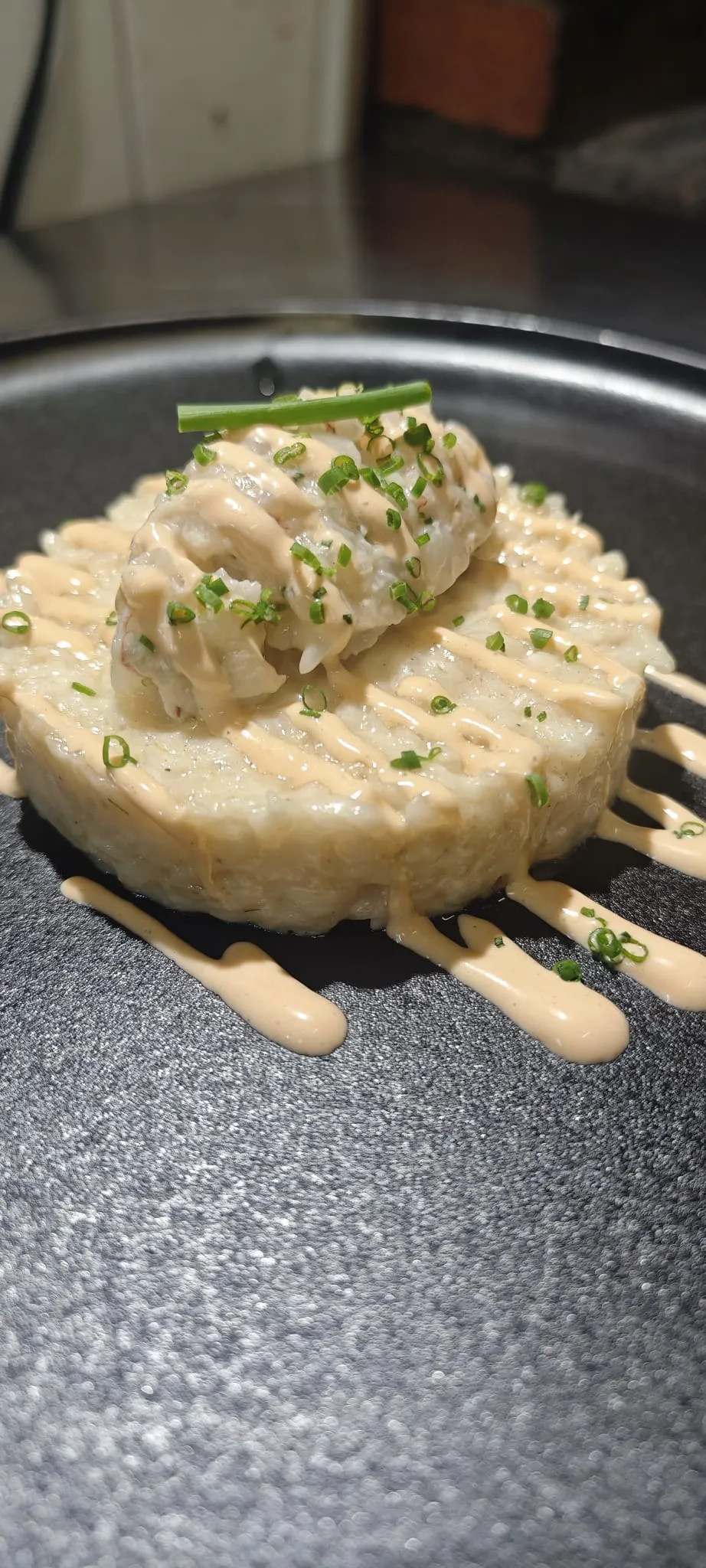 Un timbal lligat coronat amb llagostí, salsa rosada i cebollí, en un plat fosc
