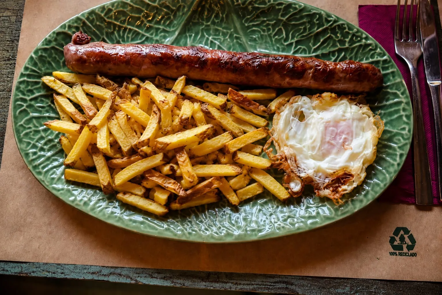 Botifarra a la brasa amb patates i ou ferrat, servida en una plata verda